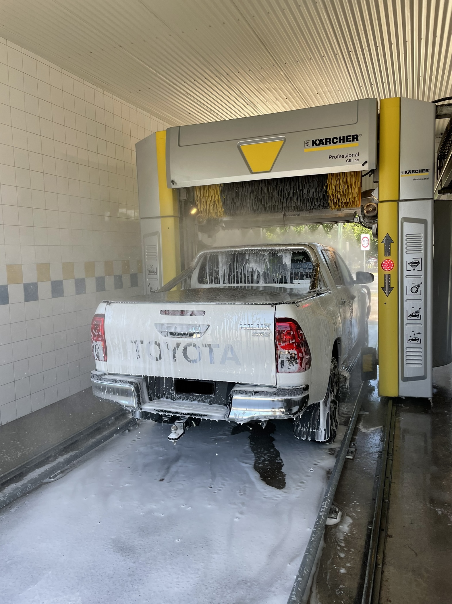 A Toyota HiLux covered in foam under the Karcher gantry inside the automatic bay