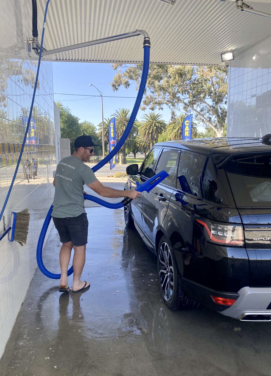 An attendant washing a vehicle by hand with a foam lance in an open bay at Swift Car Wash